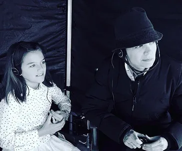 Child sitting with an adult wearing a hat, both with headphones, in a black and white photo.