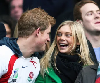 A couple smiling at each other while attending a sporting event, dressed casually among a crowd.