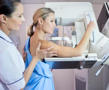 Woman undergoing a mammogram, assisted by a healthcare professional in a medical setting.