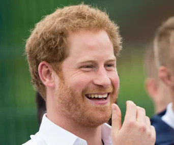 A man with red hair and a beard laughs joyfully outdoors.