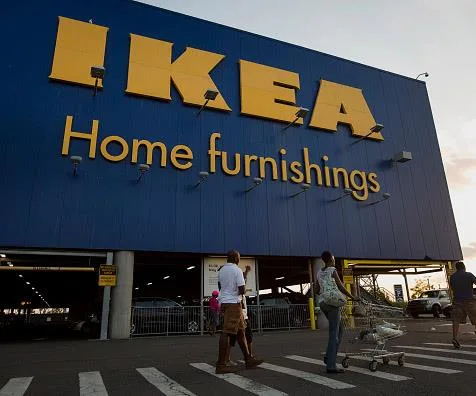 IKEA store entrance with people walking and a shopping cart, blue facade with yellow logo and "Home furnishings" text.