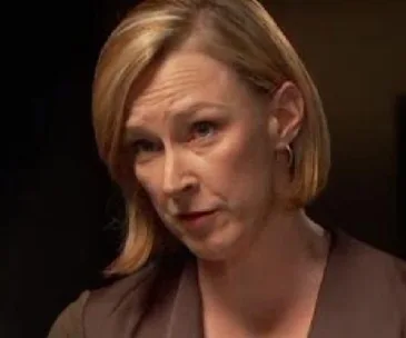 Leigh Sales in a focused interview setting, looking attentive and serious, wearing a brown top with a dark background.