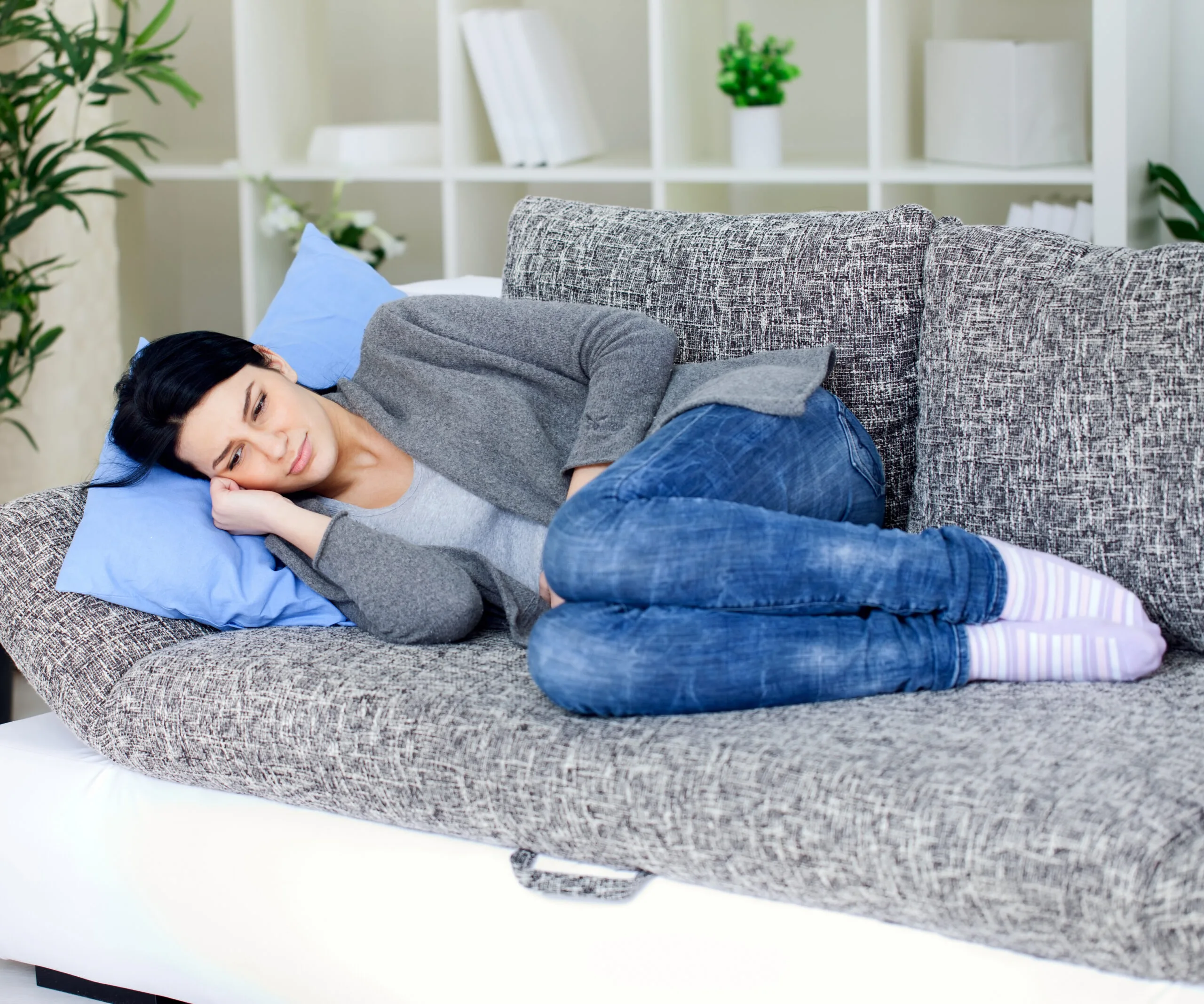 Woman lying on a couch, wearing jeans and a sweater, looking thoughtful and relaxed.