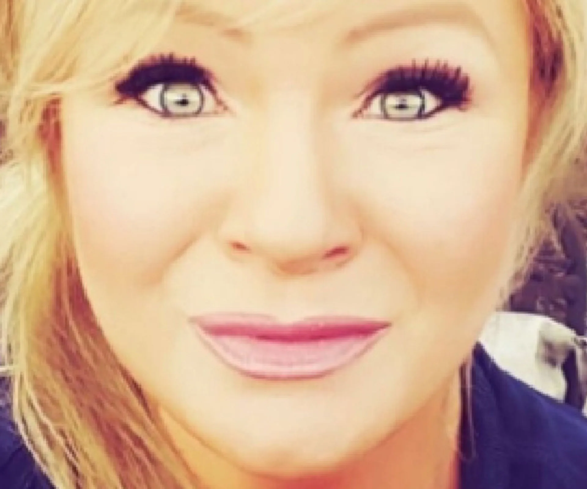 Close-up of a woman with blonde hair and bright eyes, wearing makeup and smiling slightly.