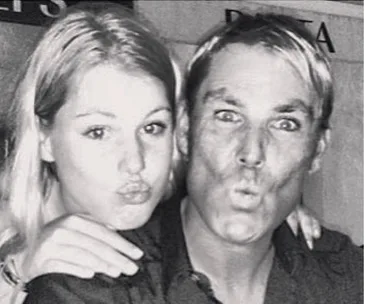 A man and a woman share a playful moment, making kissy faces at the camera, with their arms around each other.