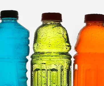 Three colorful sports drink bottles in blue, green, and orange with condensation on them against a white background.