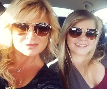 Two women wearing sunglasses smiling inside a car.