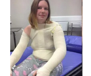 Woman in full upper body bandages and pajamas, sitting on a hospital bed.