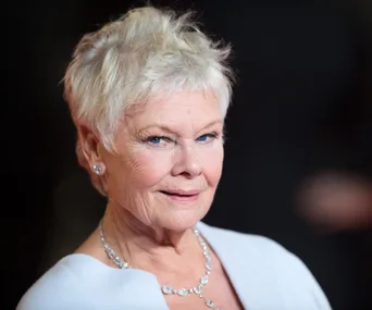 Elderly woman with short white hair and elegant necklace, smiling slightly at a formal event.