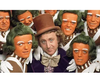Willy Wonka surrounded by Oompa Loompas, from the film "Willy Wonka & the Chocolate Factory," wearing colorful costumes.