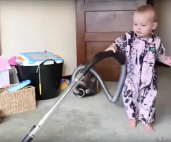 Toddler in pajamas using a vacuum cleaner in a living room setting.