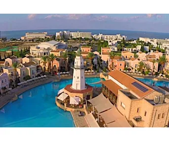 Aerial view of a Cyprus resort with a central lighthouse, surrounded by a pool and Mediterranean-style buildings.