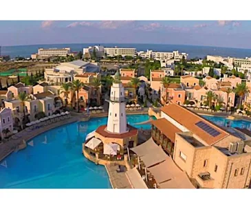 Aerial view of a Cyprus resort with a central lighthouse, surrounded by a pool and Mediterranean-style buildings.