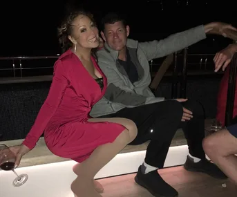 A woman in a red dress and a man in casual wear sit together on a bench at night, with a wine glass nearby.