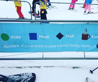 "Banner at a ski resort with symbols for 'Kids', 'Mum', 'Dad', and a coffee cup, promoting Toyota Kluger for snow-loving families."