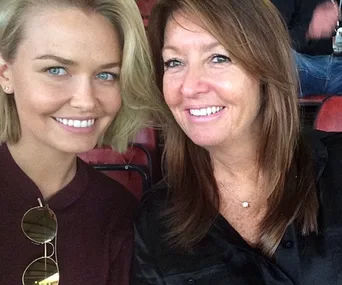 Two women sitting closely in a stadium, smiling at the camera.