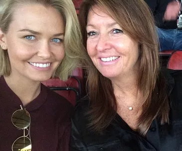 Two women sitting closely in a stadium, smiling at the camera.