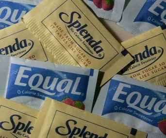 Packets of artificial sweeteners, including Splenda and Equal, scattered on a surface.