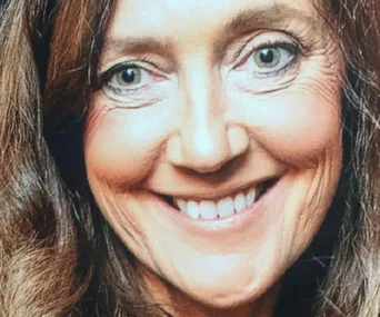 A woman with long brown hair smiling. Her eyes are light-colored and she's looking directly at the camera.