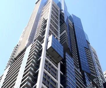 Tall modern skyscraper with various balconies and glass windows under a clear blue sky.