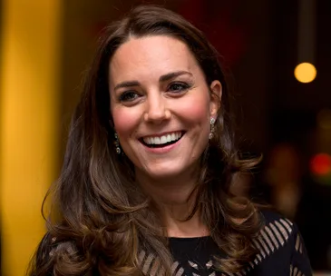 Smiling woman with long brown hair wearing elegant earrings and a patterned black top.