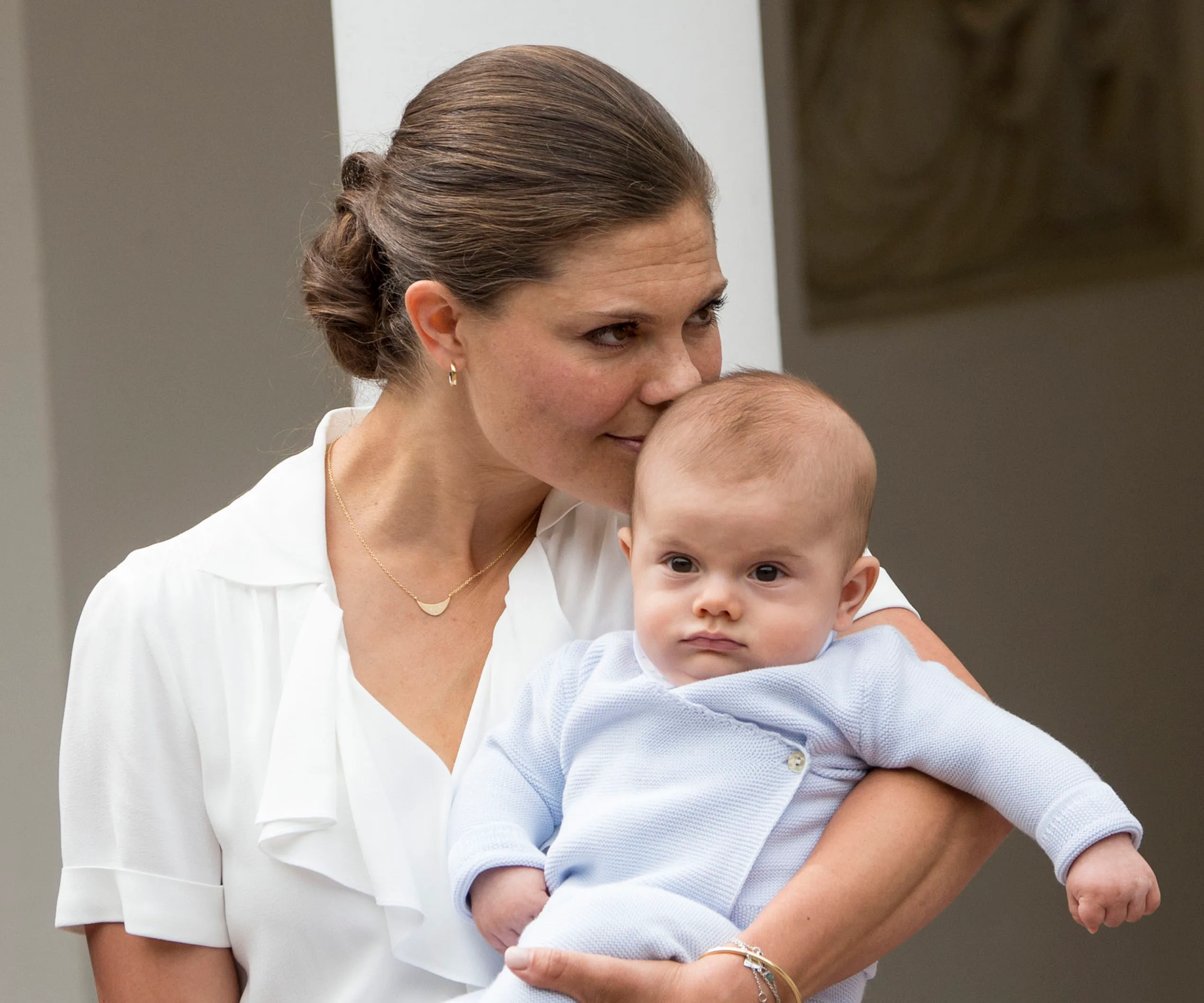 Mother holds baby affectionately; mother in a white blouse, baby in light blue outfit.