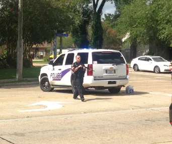 Police officer stands by LSU Police SUV with flashing lights on a street.