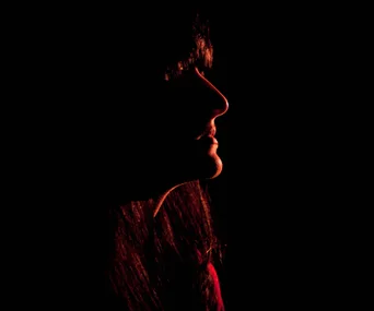 Shadowed profile silhouette of a woman against a dark background.
