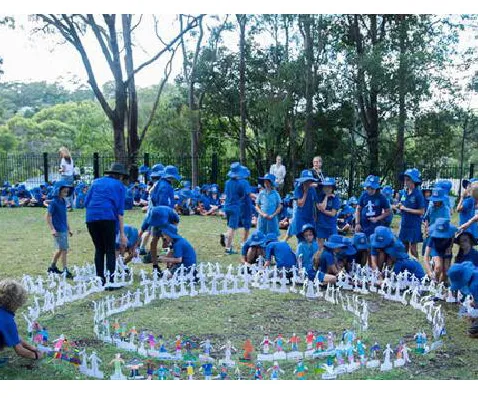 Children in blue uniforms participate in an outdoor activity, arranging paper figures in circles on grassy ground.