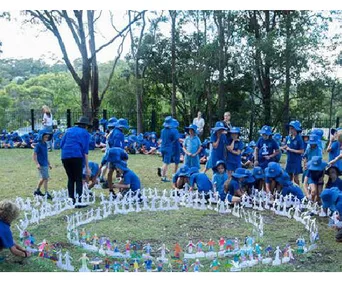 Children in blue uniforms participate in an outdoor activity, arranging paper figures in circles on grassy ground.