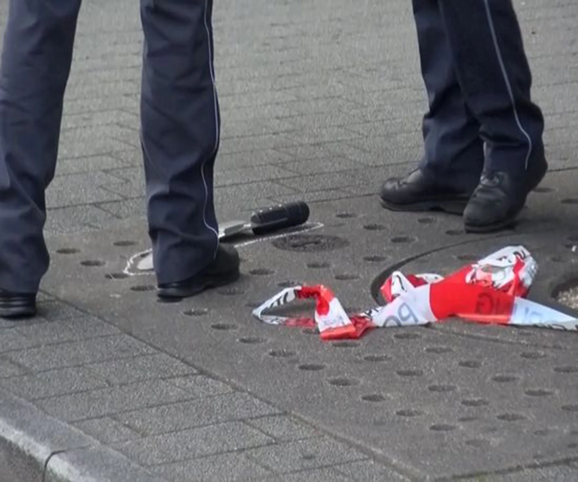Police officers stand near a machete and a red and white cloth on the pavement.