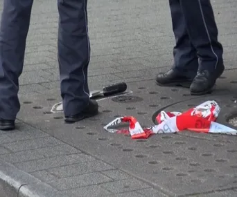 Police officers stand near a machete and a red and white cloth on the pavement.