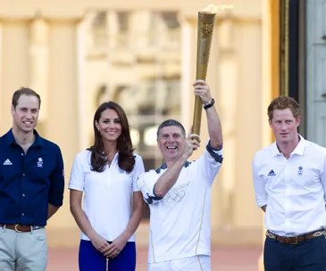 "Three people standing with a man holding the Olympic torch, smiling at an event."