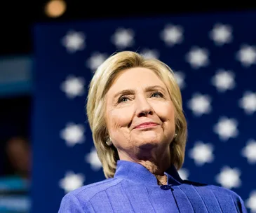 Hillary Clinton stands confidently against a backdrop of stars, wearing a blue jacket, making history with her nomination.