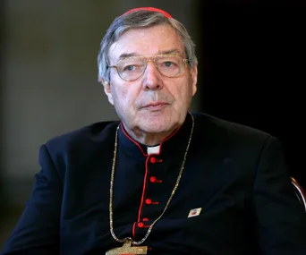 A cardinal in clerical attire and glasses, looking forward.