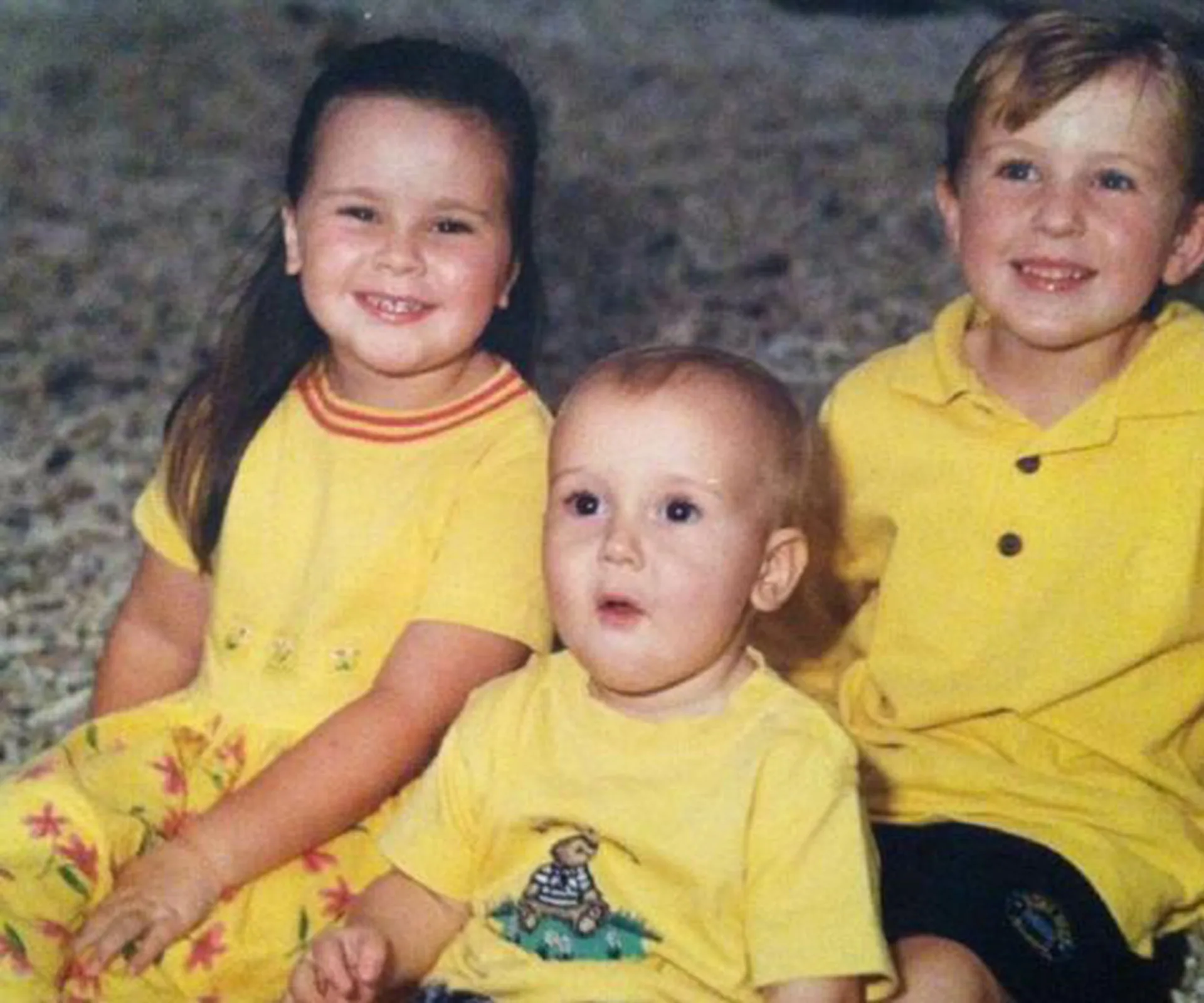 Young children in yellow outfits sitting on a textured surface, smiling and looking at the camera.