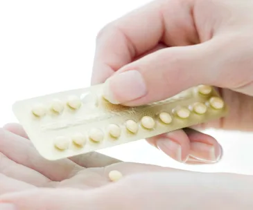 Person removing a pill from a blister pack, close-up of hands.