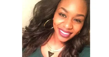 Smiling woman with dark hair and hoop earrings, wearing a green outfit and necklace, facing the camera.