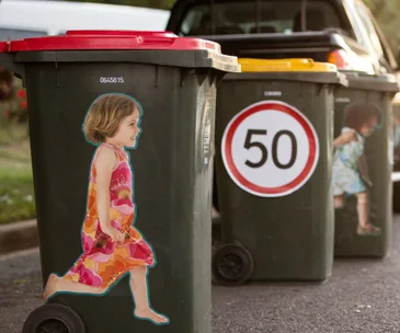 Stickers of children on wheelie bins with various lid colors and a speed limit sign, aiming to enhance child safety awareness.
