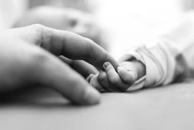 Close-up of an adult hand gently holding a baby's hand, symbolizing care and connection.