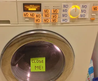 Washing machine with sticky notes saying "NO" around the controls and "CLOSE ME!" on the door.