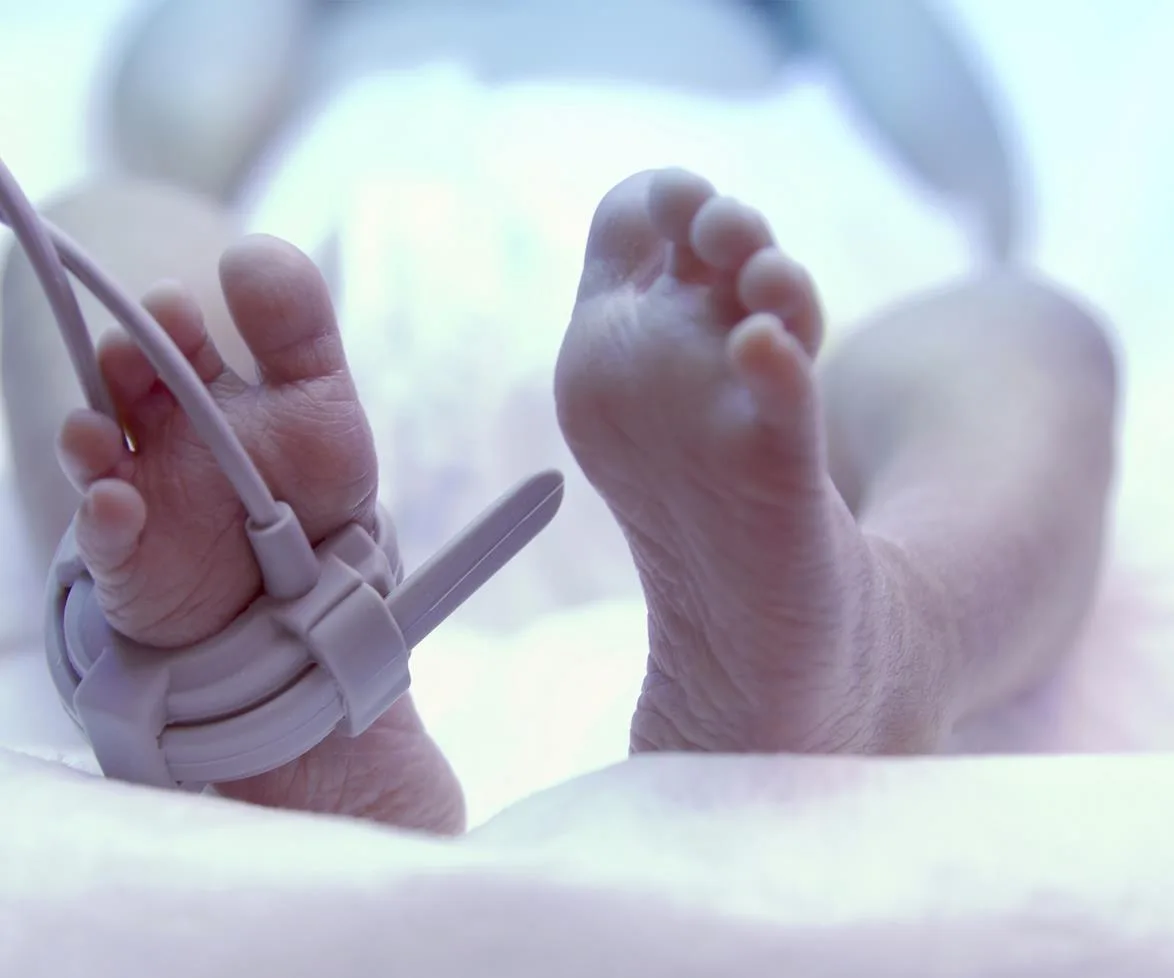 Close-up of newborn baby’s feet in a hospital, with a monitoring device attached.