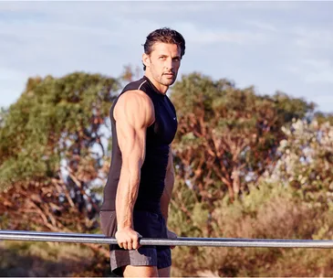 Man in athletic wear performing dips on parallel bars outdoors, with trees in the background.