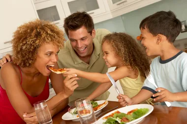 Family enjoying a meal at home, smiling and sharing a slice of pizza.