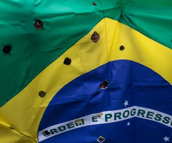 Brazilian flag with bullet holes, peering eyes visible through holes.