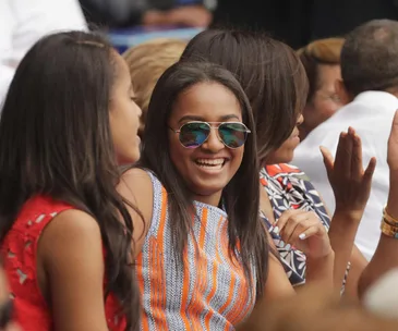Young woman wearing sunglasses smiles and chats with friends at an outdoor event.