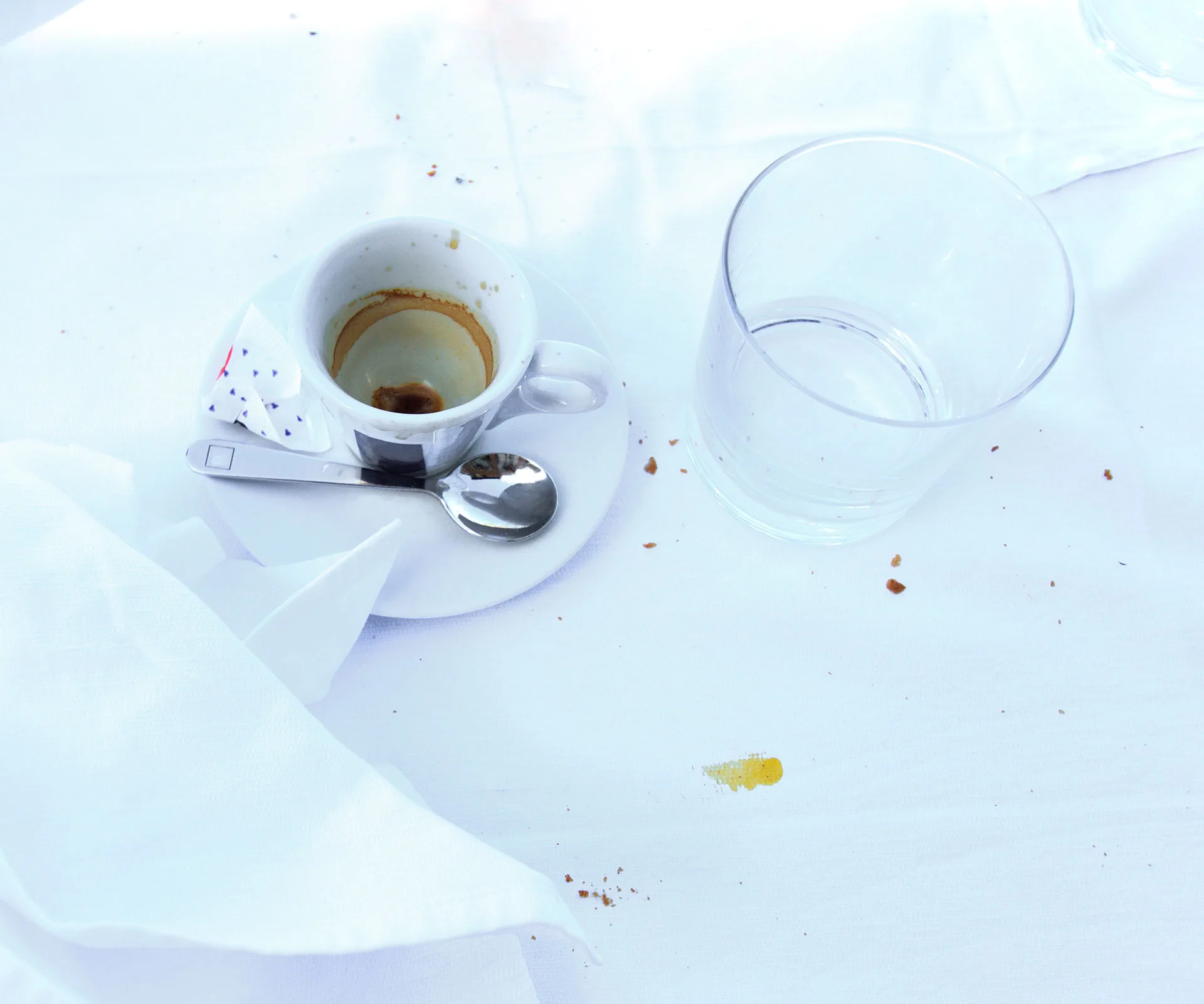 Empty coffee cup and water glass on a table, with scattered crumbs and a napkin.