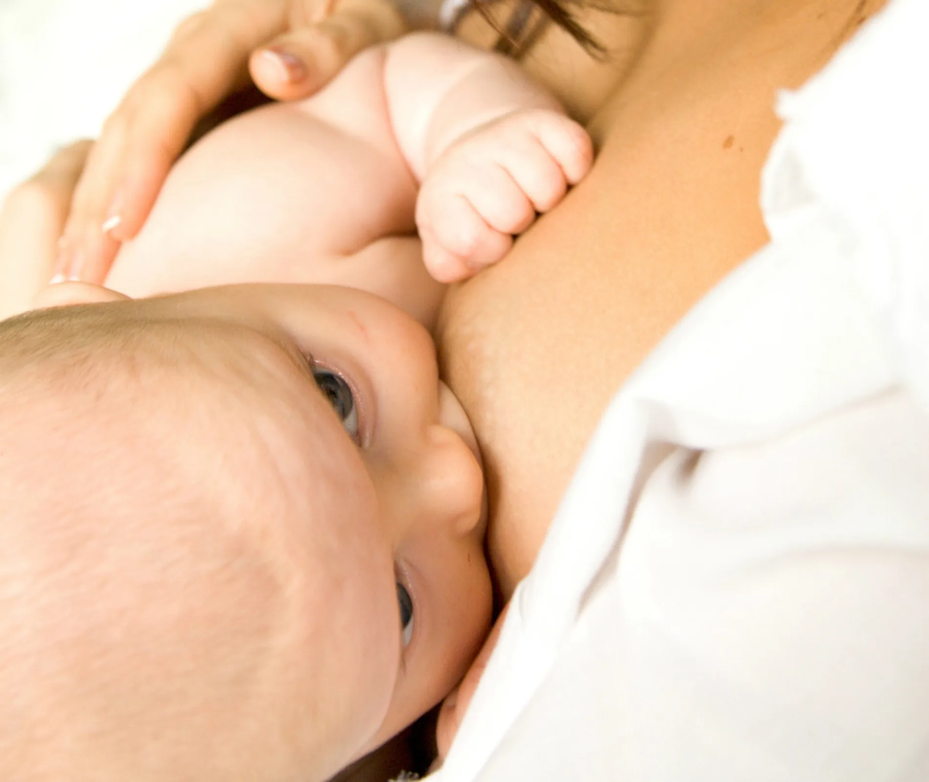 A baby breastfeeding from a woman's chest, close-up view.