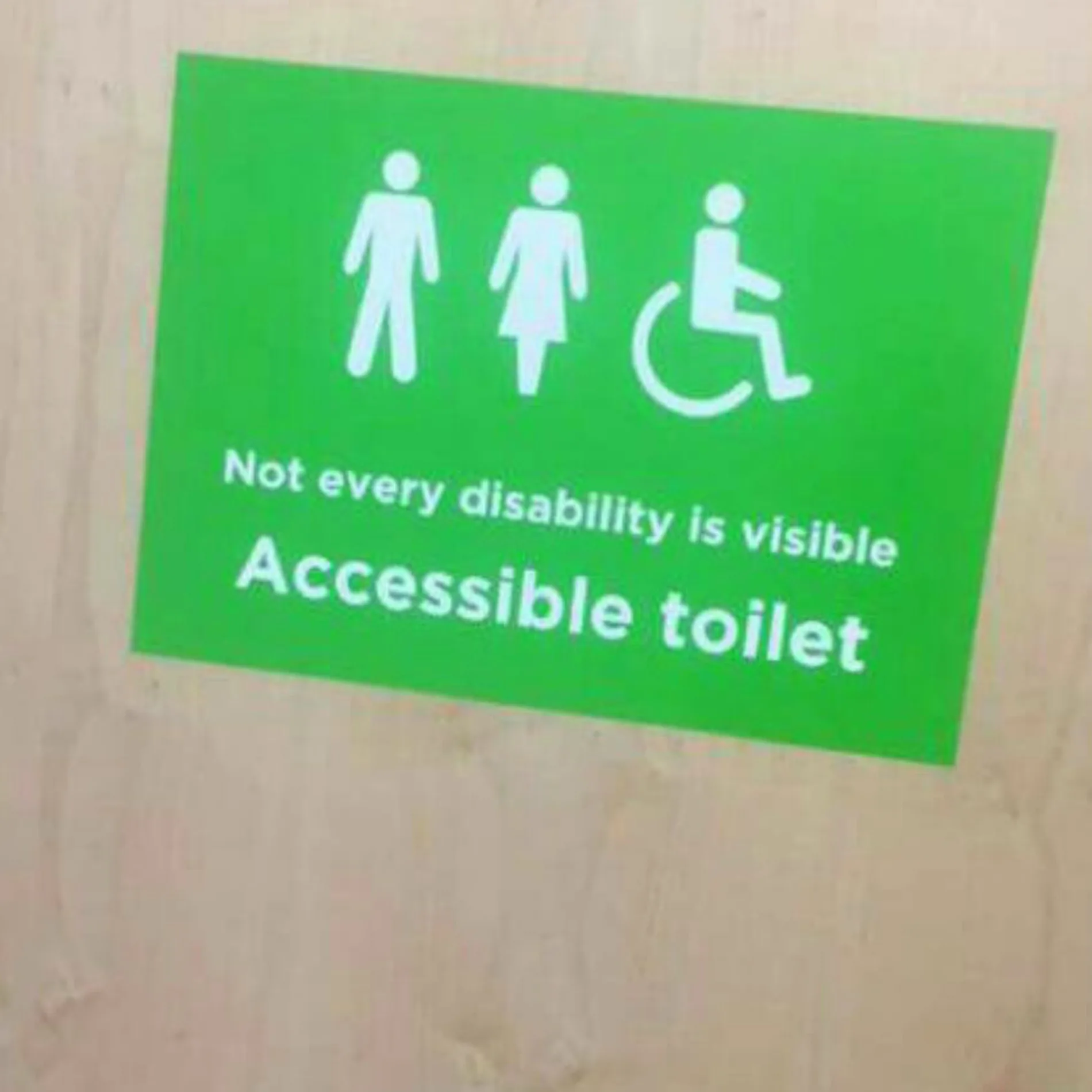 Accessible toilet sign reading "Not every disability is visible" with male, female, and wheelchair symbols.