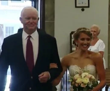 Bride smiles while walking down the aisle arm-in-arm with her father's heart transplant recipient.